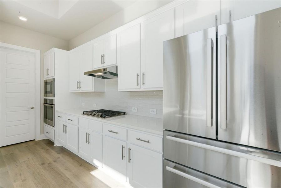 Kitchen featuring appliances with stainless steel finishes, white cabinets, light wood-style floors, decorative backsplash, and recessed lighting