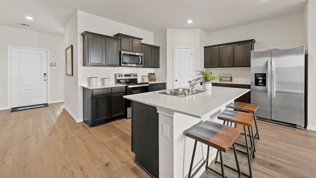 The kitchen features dark wood cabinetry, white countertops, and stainless steel appliances The kitchen features dark wood cabinetry, white countertops, and stainless steel appliances