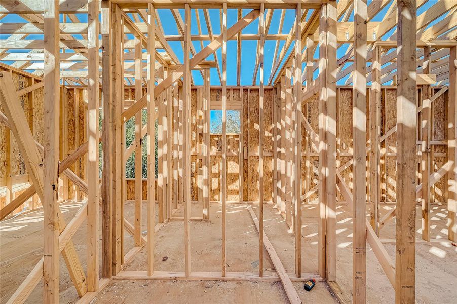 This photo shows a house under construction, featuring wooden framing and exposed beams against a clear blue sky. It's ready for further development, offering a glimpse of potential layout and design.