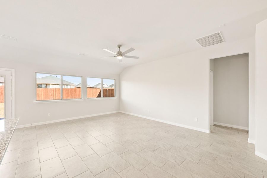 Empty living room with vaulted ceiling, ceiling fan, tile floors, and large windows facing backyard fence. Empty living room with vaulted ceiling, ceiling fan, tile floors, and large windows facing backyard fence.