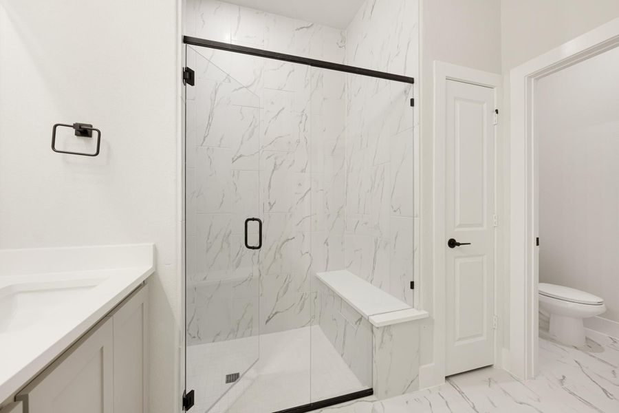 Bathroom with glass-enclosed shower, marble tile walls, built-in bench, and black hardware accents