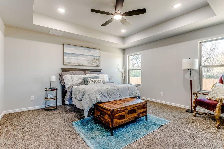 Bedroom with ceiling fan, a raised ceiling, and carpet floors