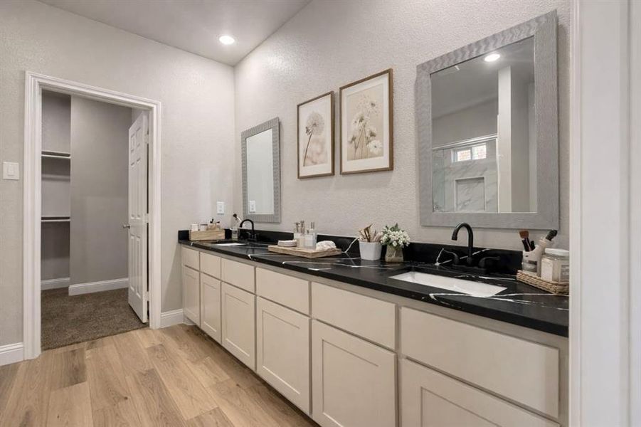 Bathroom with double vanity, light wood-style flooring, an enclosed shower, and a spacious closet