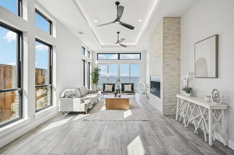 Open concept family room with gas-serviced fireplace, 12 foot ceilings, LED uplighting in tray ceiling feature, and floor to ceiling windows welcoming an abundance of natural light all centered around the Lake Ray Hubbard views.