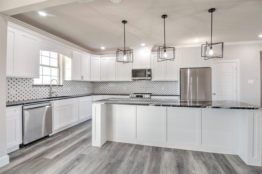Kitchen with stainless steel appliances, white cabinetry, pendant lighting, dark stone counters, and ornamental molding