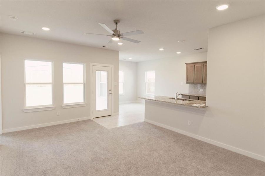 Unfurnished living room with light carpet, ceiling fan, and sink