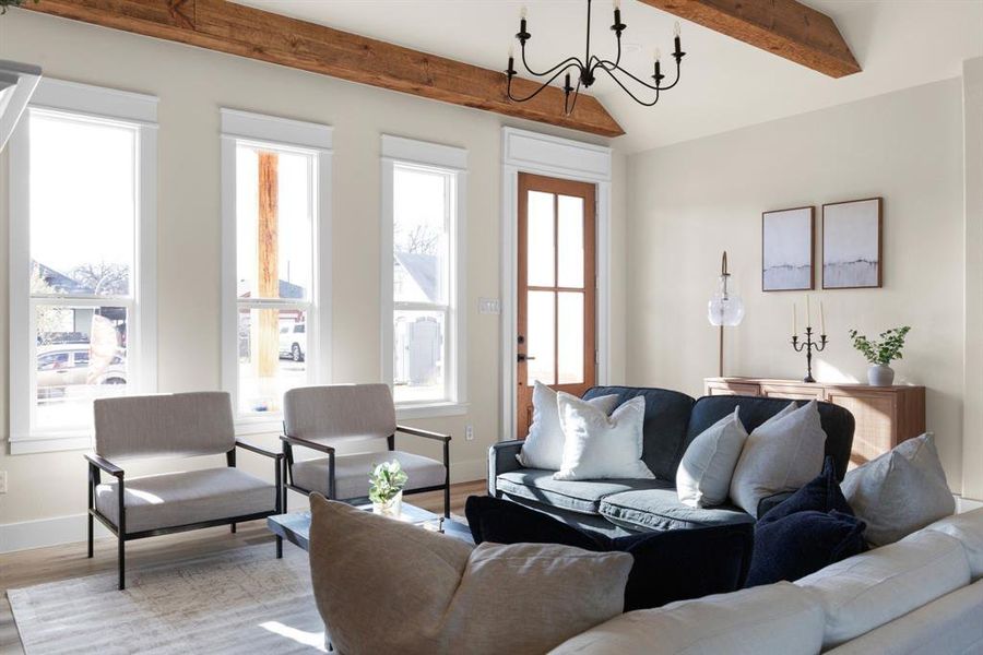 Living room with lofted ceiling with beams, light wood-type flooring, a wealth of natural light, and an inviting chandelier