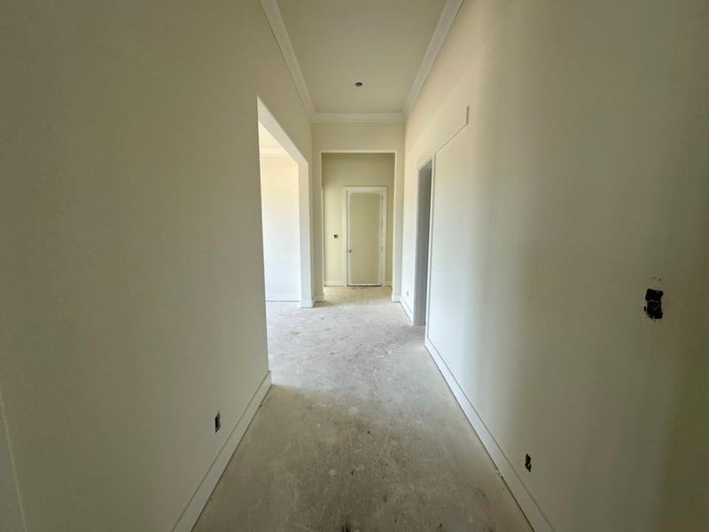 Hallway featuring neutral wall tones, crown molding, wide baseboards, and framed doorways