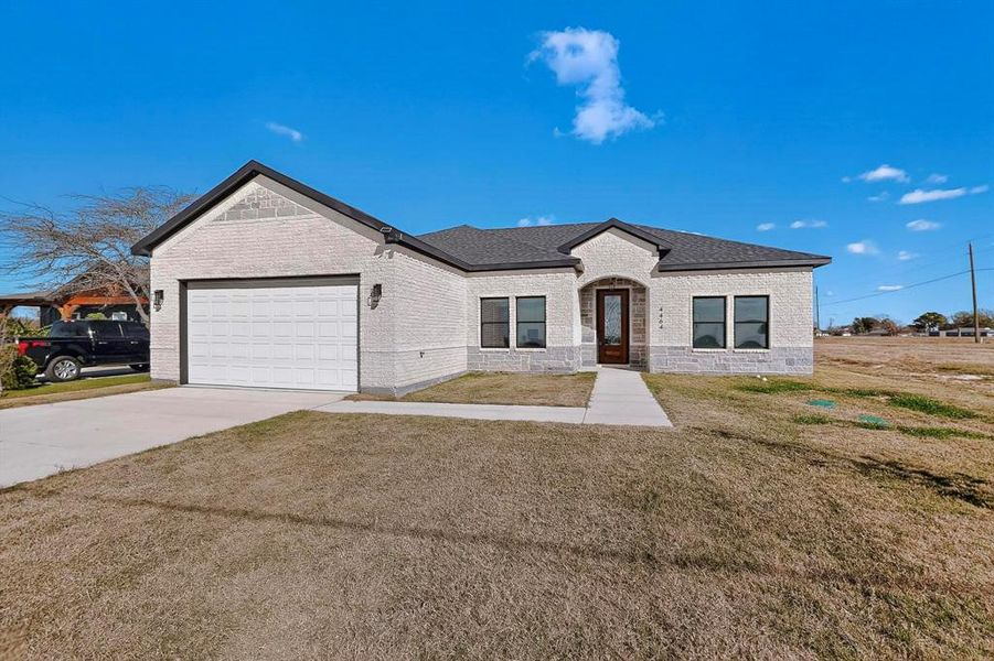 View of front of house featuring driveway, a front lawn, brick siding, and an attached garage