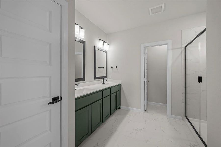 Bathroom featuring double vanity, a marble finish shower, and light marble finish floors