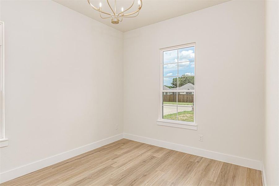 Bright interior space featuring a window with grid panes, wood-finish flooring, white baseboards, and a gold-toned chandelier