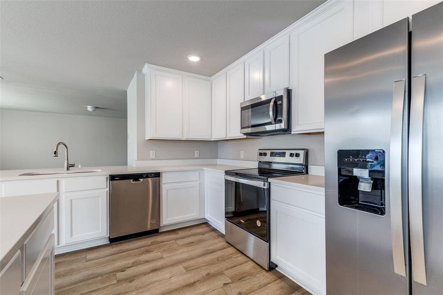 Kitchen with white cabinetry, sink, appliances with stainless steel finishes, and light hardwood / wood-style flooring