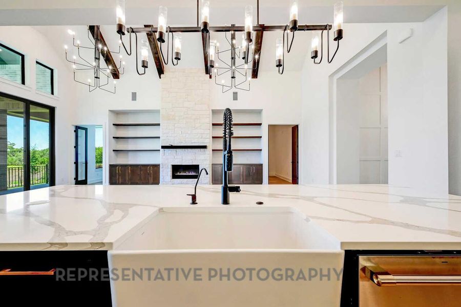 Kitchen featuring light stone countertops, open floor plan, an island with sink, a chandelier, and a high ceiling Kitchen featuring light stone countertops, open floor plan, an island with sink, a chandelier, and a high ceiling