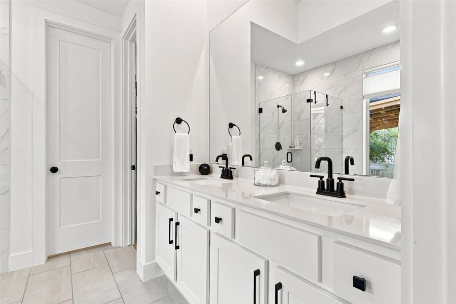 Clean lines and a spacious dual vanity define this modern, stone-countered bathroom oasis.