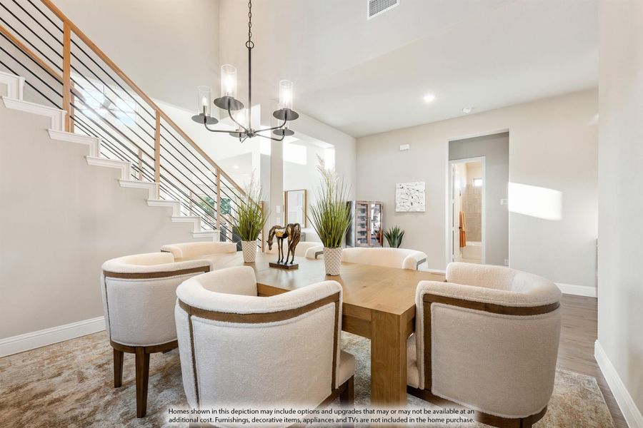 Dining room with wood table, cream barrel chairs, pendant chandelier, and open staircase with metal railing nearby. Dining room with wood table, cream barrel chairs, pendant chandelier, and open staircase with metal railing nearby.