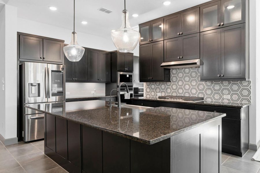Gourmet kitchen with oversized island, granite countertops, pendant lighting, and custom cabinetry.