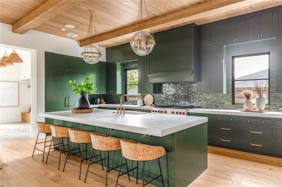 Kitchen featuring a wooden ceiling with exposed beams, light wood-type flooring, light countertops, tasteful backsplash, and a kitchen island with sink