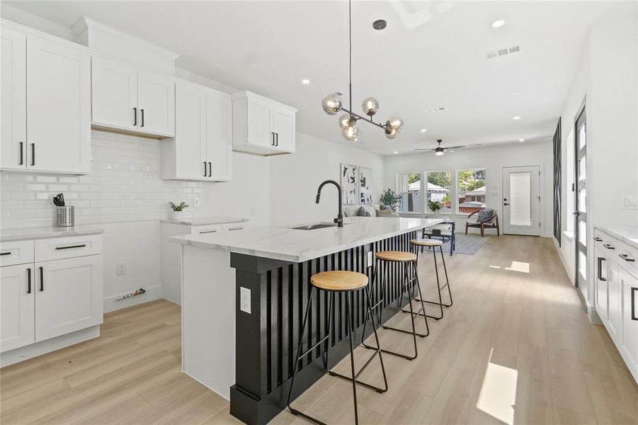 Kitchen with white cabinets, light stone counters, backsplash, light wood-type flooring, and a breakfast bar area Kitchen with white cabinets, light stone counters, backsplash, light wood-type flooring, and a breakfast bar area