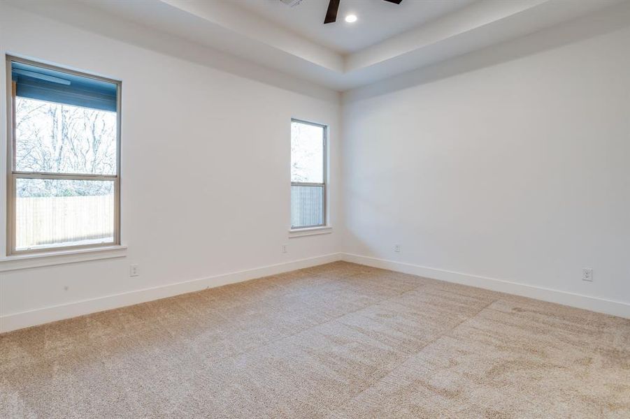 Spare room featuring light colored carpet, ceiling fan, and a raised ceiling