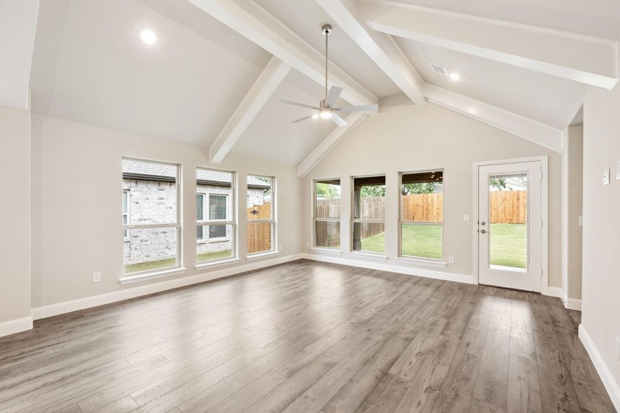 Open living area with vaulted ceiling, white wood beams, ceiling fan, hardwood floors, and backyard-facing windows and door