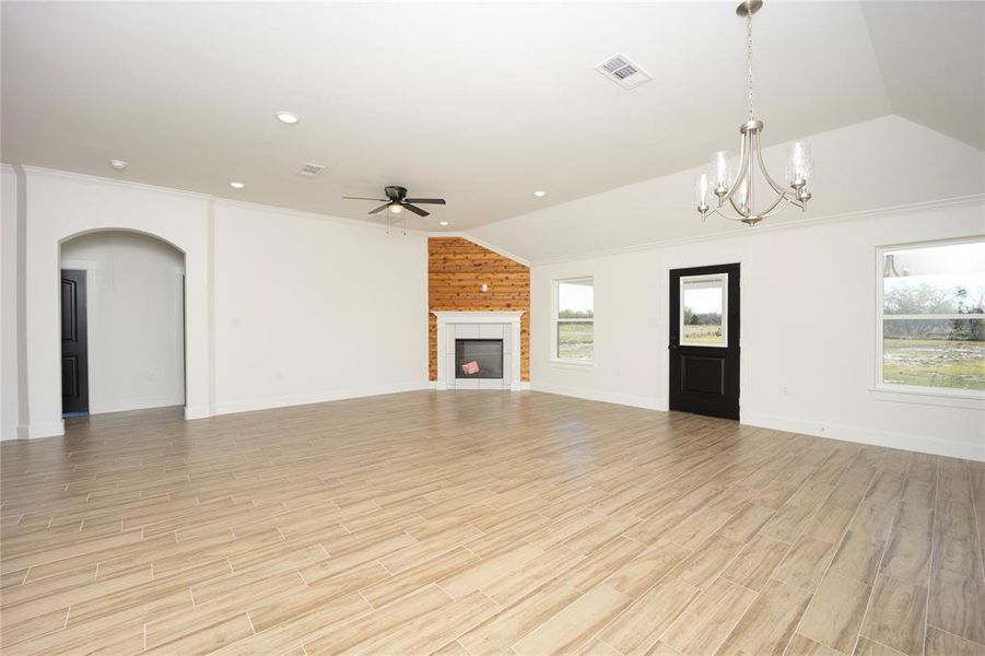 Unfurnished living room featuring lofted ceiling, a chandelier, ornamental molding, light wood finished floors, and a fireplace