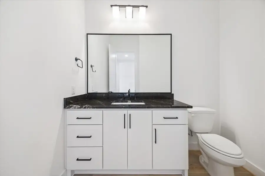 Bold and minimal, the half bath features a dramatic black stone countertop, sleek hardware, and modern lighting offering a polished, stylish touch for guests. Bold and minimal, the half bath features a dramatic black stone countertop, sleek hardware, and modern lighting offering a polished, stylish touch for guests.