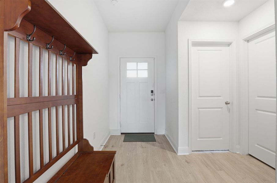 Entryway featuring light wood-finish flooring, white trim, and a built-in wooden hall tree with storage and coat hooks