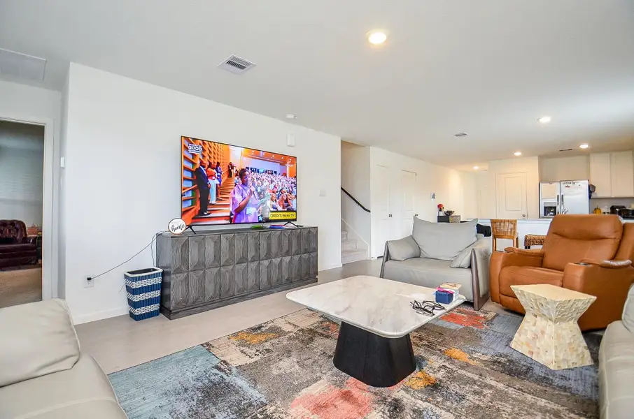 This spacious bedroom features a large bed with an elegant tufted headboard, neutral carpeting, and ample natural light. A cozy red armchair and bedside tables provide comfort and functionality, while a walk-in closet is accessible through an adjacent door.