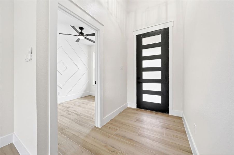 Entryway featuring a modern black door with frosted glass panels, wood-finish flooring, and white baseboards Entryway featuring a modern black door with frosted glass panels, wood-finish flooring, and white baseboards