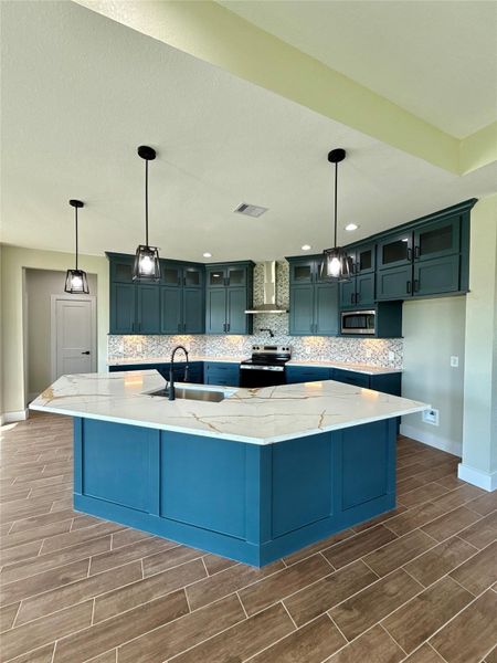 This kitchen features a modern design with rich teal cabinetry, a spacious marble countertop island with a sink, and elegant pendant lighting. The backsplash adds texture, and the wood-look tile flooring complements the contemporary style. This kitchen features a modern design with rich teal cabinetry, a spacious marble countertop island with a sink, and elegant pendant lighting. The backsplash adds texture, and the wood-look tile flooring complements the contemporary style.