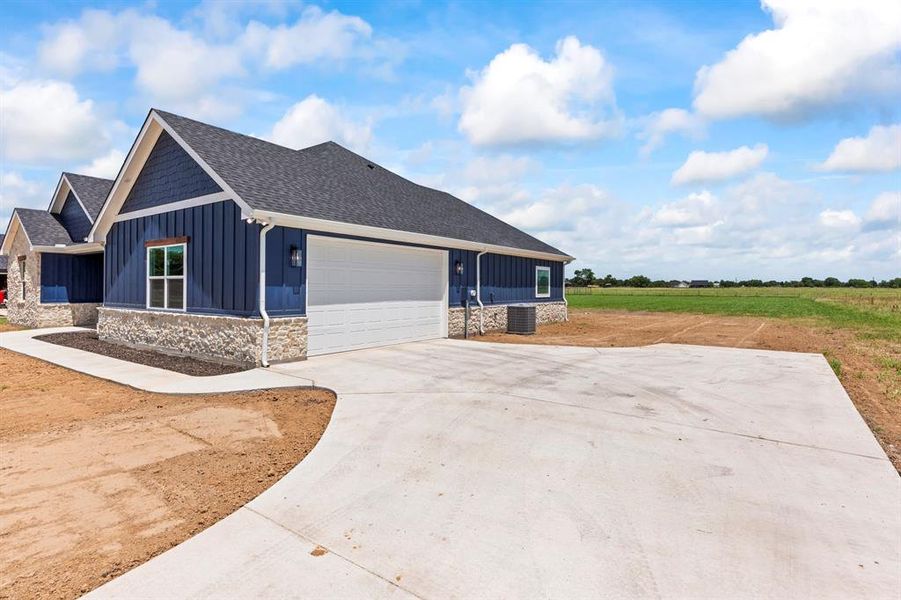 View of property exterior featuring board and batten siding, stone siding, a garage, a shingled roof, and concrete driveway