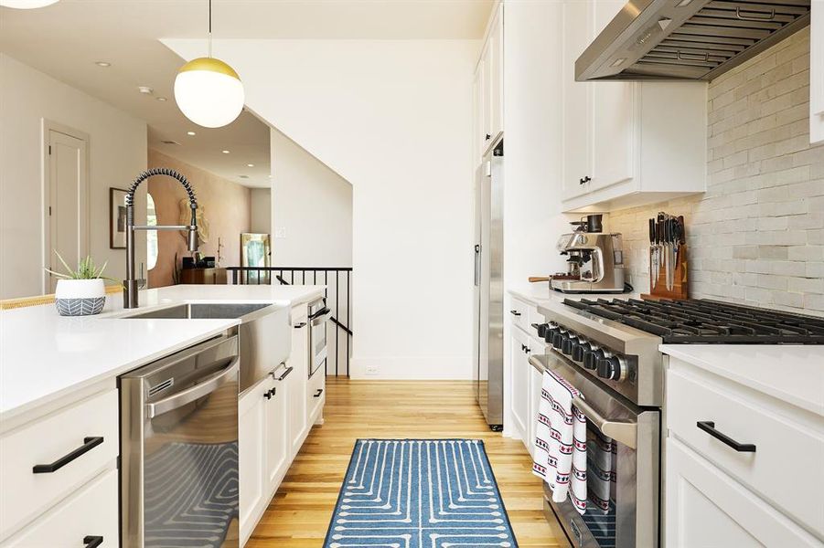 Brand new appliances with stainless steel finishes, exhaust hood, white cabinets, light wood-style floors, and pendant lighting