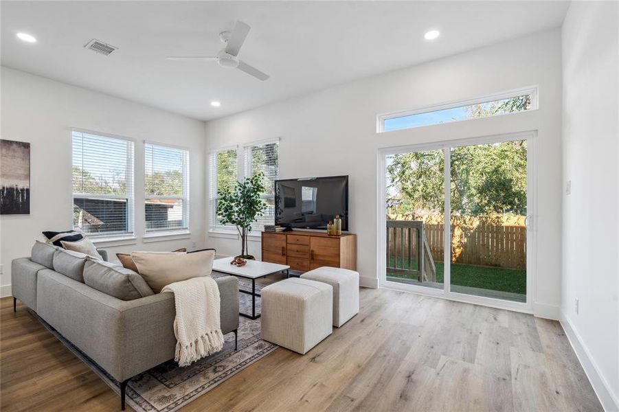 Bright and airy living room featuring large windows, sliding glass doors for easy access to the backyard, and a cozy yet modern setup perfect for relaxing or entertaining.