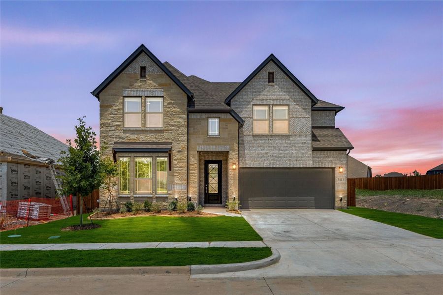 Two-story brick and stone home with two-car garage, large windows, and manicured front lawn at dusk Two-story brick and stone home with two-car garage, large windows, and manicured front lawn at dusk