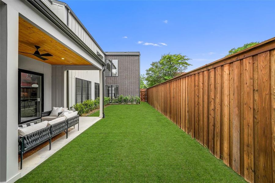 Expansive green lawn alongside a covered patio featuring a wood-panel ceiling and ceiling fan