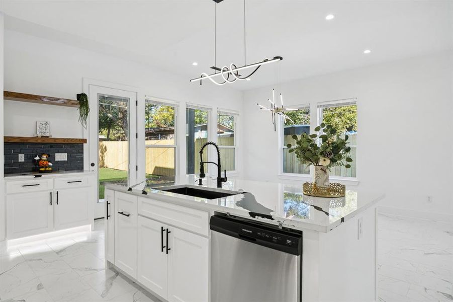 Kitchen featuring light marble finish floors, dishwasher, an island with sink, backsplash, and recessed lighting