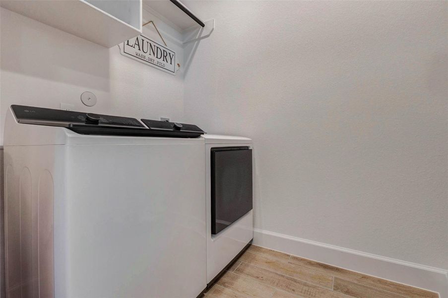Laundry room with a washer and dryer. The space features white walls, light wood flooring, and a shelf above the appliances for storage. Laundry room with a washer and dryer. The space features white walls, light wood flooring, and a shelf above the appliances for storage.
