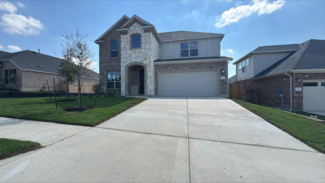 French country inspired facade with stone siding, driveway, and an attached garage