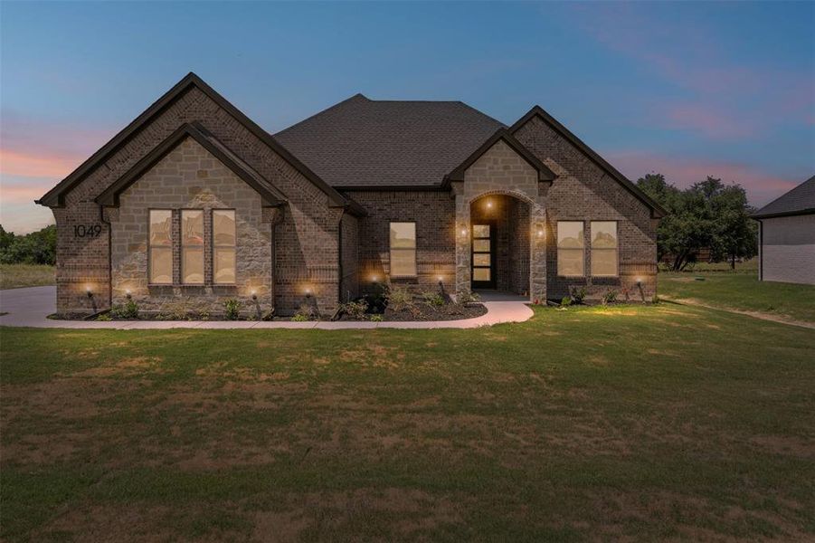 French country home featuring stone siding, brick siding, and a front yard French country home featuring stone siding, brick siding, and a front yard