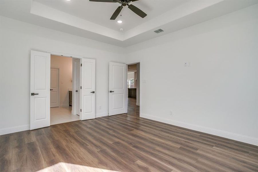 Unfurnished bedroom with a raised ceiling, wood finished floors, recessed lighting, and a ceiling fan