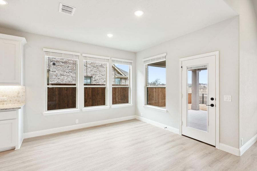 Bright breakfast nook with light wood floors, three windows, and glass door leading to covered patio Bright breakfast nook with light wood floors, three windows, and glass door leading to covered patio