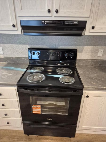 Kitchen view of black electric range, range hood, and dark countertops