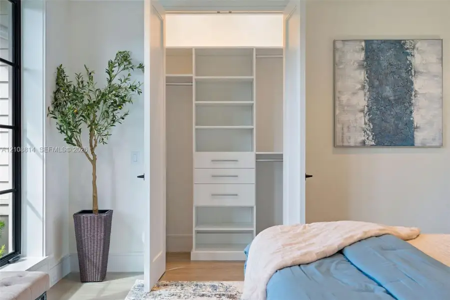 Custom-built closet featuring white cabinetry, tiered shelving, integrated drawers with metallic pulls, and dual hanging rods Custom-built closet featuring white cabinetry, tiered shelving, integrated drawers with metallic pulls, and dual hanging rods