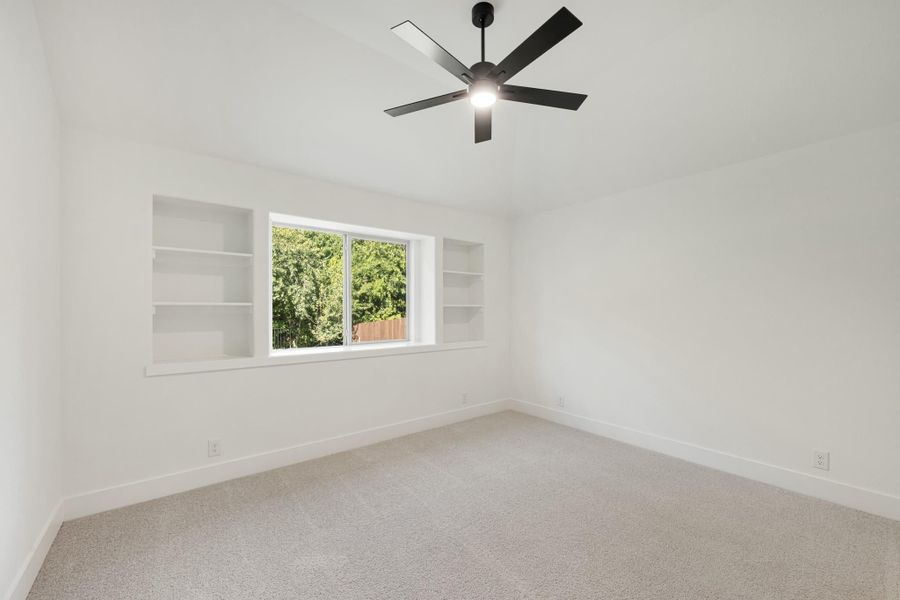 Empty bedroom with carpet, black ceiling fan, and built-in shelves flanking a center window