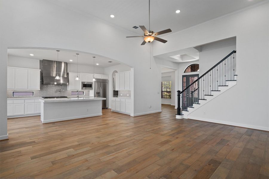 Open-concept living space featuring wood-finish flooring, a contemporary kitchen with a large island, stainless steel appliances, and white cabinetry