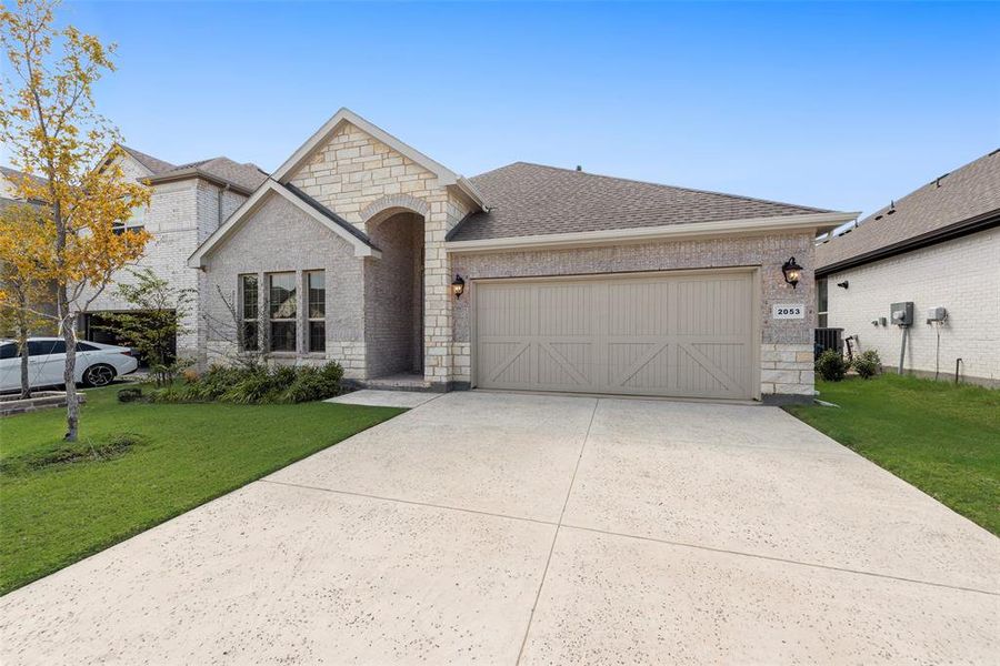 French country inspired facade with stone siding, a front lawn, brick siding, driveway, and a shingled roof