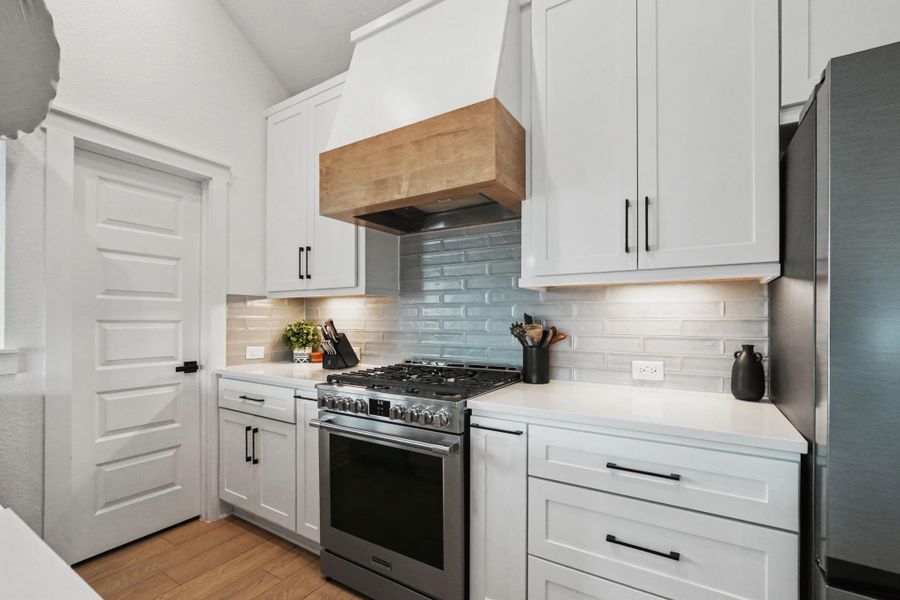 Beautifully designed kitchen showcasing custom cabinetry, sleek quartz countertops, and a professional-grade gas range with statement vent hood. Stylish tile backsplash and under-cabinet lighting add warmth and a polished, modern finish.