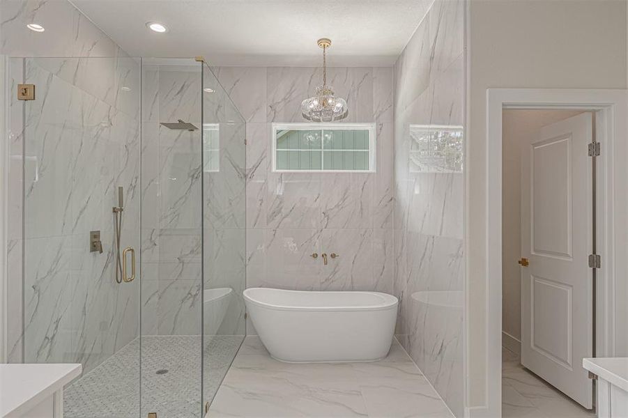 Freestanding soaking tub with wall-mounted fixtures, framed by large format marble-look tile
