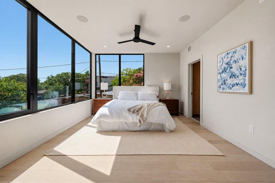 Floor-to-ceiling windows offer captivating neighborhood views from this serene primary bedroom with hardwood flooring. Floor-to-ceiling windows offer captivating neighborhood views from this serene primary bedroom with hardwood flooring.
