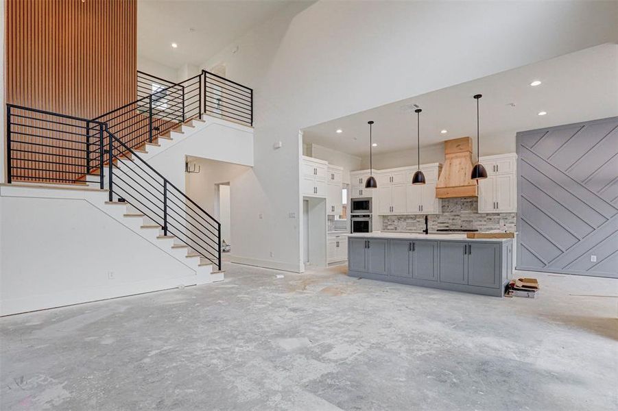 Kitchen with premium range hood, a large island with sink, tasteful backsplash, decorative light fixtures, and white cabinetry